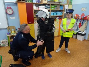 Dzielnicowy prezentuje uczniom policyjny sprzęt