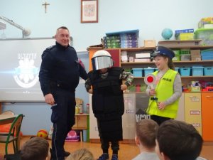 Dzielnicowy prezentuje uczniom policyjny sprzęt
