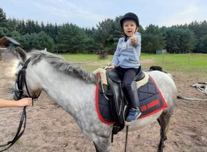 Marcel siedzi uśmiechnięty na koniu trzymając w górze kciuk lewej ręki.