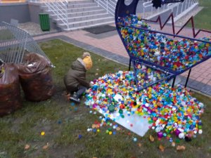 Chłopiec zbiera nakrętki, które wysypały się z pojemnika w kształcie serca stojącego przed piską komendą.