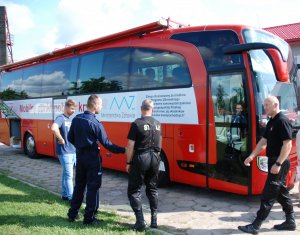 Policjanci i strażacy stoją przez autobusem honorowego krwiodawstwa.