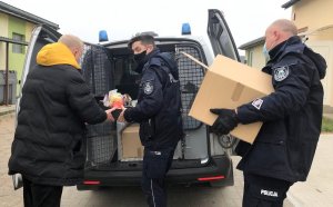 Umundurowani policjanci noszą paczki żywnościowe do oznakowanego radiowozu.