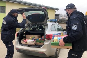 Umundurowani policjanci noszą paczki żywnościowe do oznakowanego radiowozu.