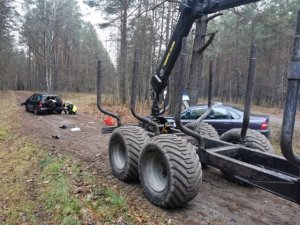 Widoczna droga gruntowa w lesie. Stoją tam pojazdy uczestniczące w zdarzeniu drogowym.