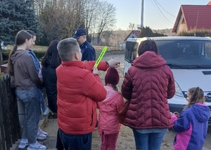 Grupka osób, a wśród nich umundurowany policjant, który rozdaje opaski odblaskowe.