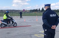 Plac manewrowy. Po prawej uczestnik turnieju jadący motorowerem . Po prawej umundurowany policjant stojący tyłem.