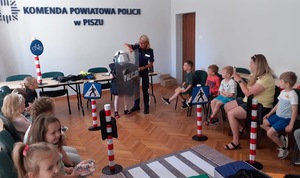 Sala, w której siedzą dzieci. Na środku policjantka pomaga jednemu z dzieci przymierzać kask.