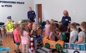 Dzieci w sali bawią się w miasteczku ruchu drogowego pod okiem policjantki.