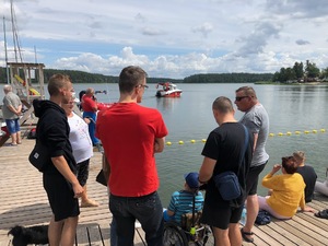 Turyści stojący na pomoście nad jeziorem, którzy obserwują pokazy ratowników i policjantów.