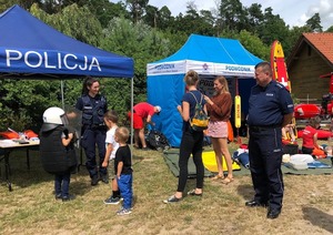 Na plaży stoją dwa namioty profilaktyczne. Przed nimi umundurowani policjanci oraz dzieci.