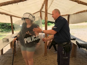 Pod namiotem policjant pomaga harcerce ubrać policyjny strój w postaci kamizelki i hełmu.