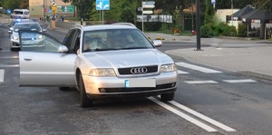 Droga. Na lewym pasie stoi przodem samochód w kolorze srebrnym, który ma otwarte drzwi od strony pasażera.