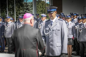 Na placu po lewej biskup, który składa gratulacje dla stojącego po prawej umundurowanego policjanta.
