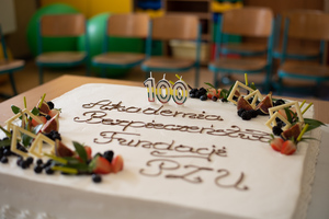 Biały tort, na którym są świeczki z cyfrą 100 i napisem - Akademia Bezpieczeństwa Fundacji PZU