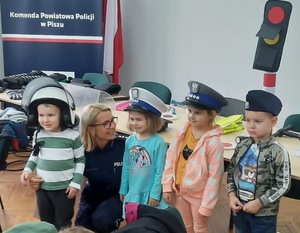 Policjantka kuca wśród trójki dzieci, które mają na sobie różne policyjne czapki.