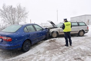 Droga zimą. Na zdjęciu widać czołowe zderzenie dwóch pojazdów. Przed nimi stoi policjant wykonujący czynności. Widać go tyłem w kamizelce odblaskowej.