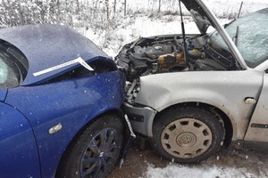 Droga zima. Z bliska widać czołowe zderzenie samochodu w kolorze niebieskim po lewe i srebrnego po prawej.