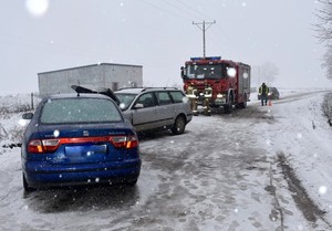 Droga zimą. Na łuku widoczne dwa samochody stuknięte przodem, a w tle wóz strażacki.