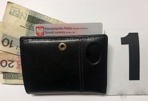 Czarny portfel, z którego wystają banknoty i dowód osobisty. Po prawej stronie czarny znacznik z numerem jeden na białym tle.