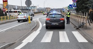 Droga- na pierwszym planie przejście dla pieszych, a za nim stojący tyłem samochód osobowy. Po prawej stronie auta stoi policjant.