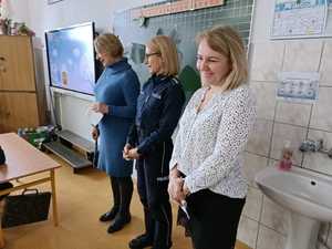 Na zdjęciu trzy kobiety stojące przed tablicą w klasie. Po środku stoi policjantka.