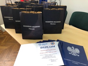 Na stole stoją granatowe torby prezentowe, a przed nimi leżą dyplomy.