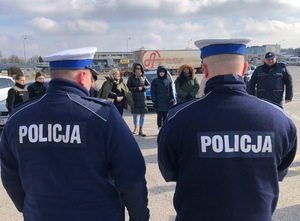 Na placu tyłem stoi dwóch policjantów, a przed nimi grupka osób.