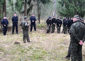 W lesie na polanie stoją przedstawiciele różnych służb.