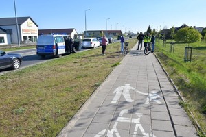 Fragment ścieżki rowerowej. W oddali widać  kilka osób.Po lewej na drodze policyjny radiowóz.