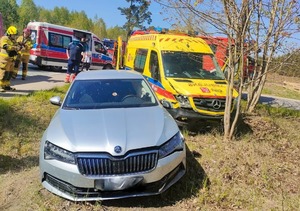 Przy drodze na łące stoi ustawiona przodem skoda, a obok niej karetka