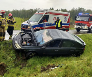 W przydrożnym rowie samochód osobowy. W tle służby ratunkowe.