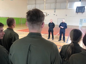 Młodzież słucha stojącego przed nimi policjanta na sali gimnastycznej