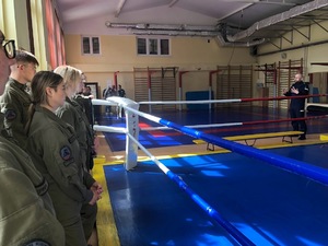 Młodzież słucha stojącego przed nimi policjanta na sali gimnastycznej.