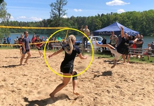 Boisko do piłki plażowej. W tle widać namiot z napisem &quot;POLICJA&quot;. Na pierwszym planie kobieta w policyjnej koszulce, która skacze do piłki.