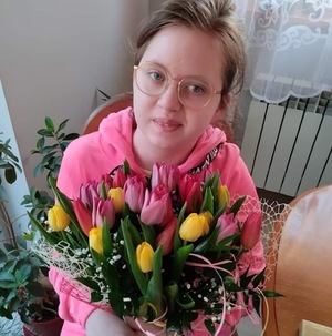 na zdjęciu uśmiechnięta dziewczynka trzymająca w rękach kwiaty