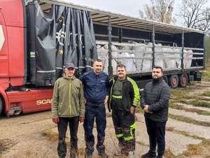 Czterech mężczyzn, w tym policjant, stojący na tle tira wyładowanego workami z kasztanami