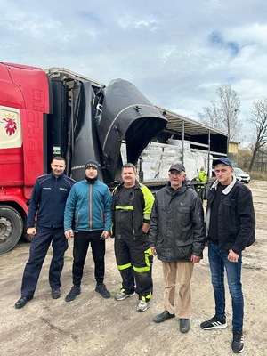 Grupa mężczyzn, w tym po lewej policjant, na tle tira z kasztanami